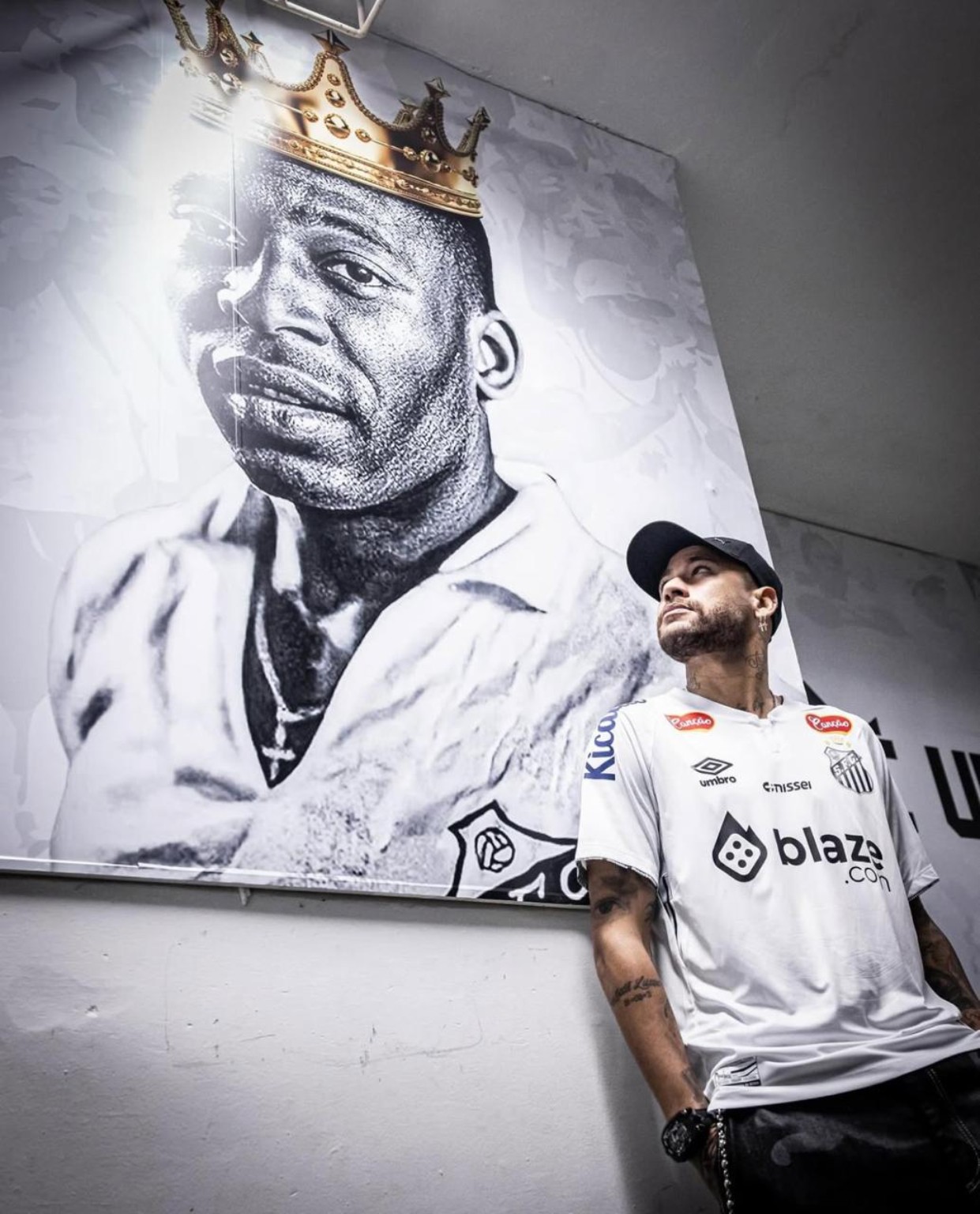 Visitante com camisa do Santos diante de retrato de Pelé com coroa.